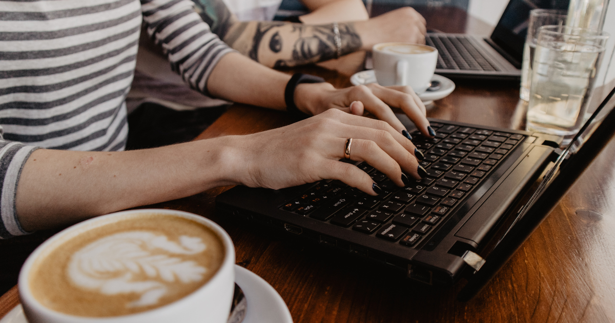 Working in a coffee shop with a latte art and tattooed arms.