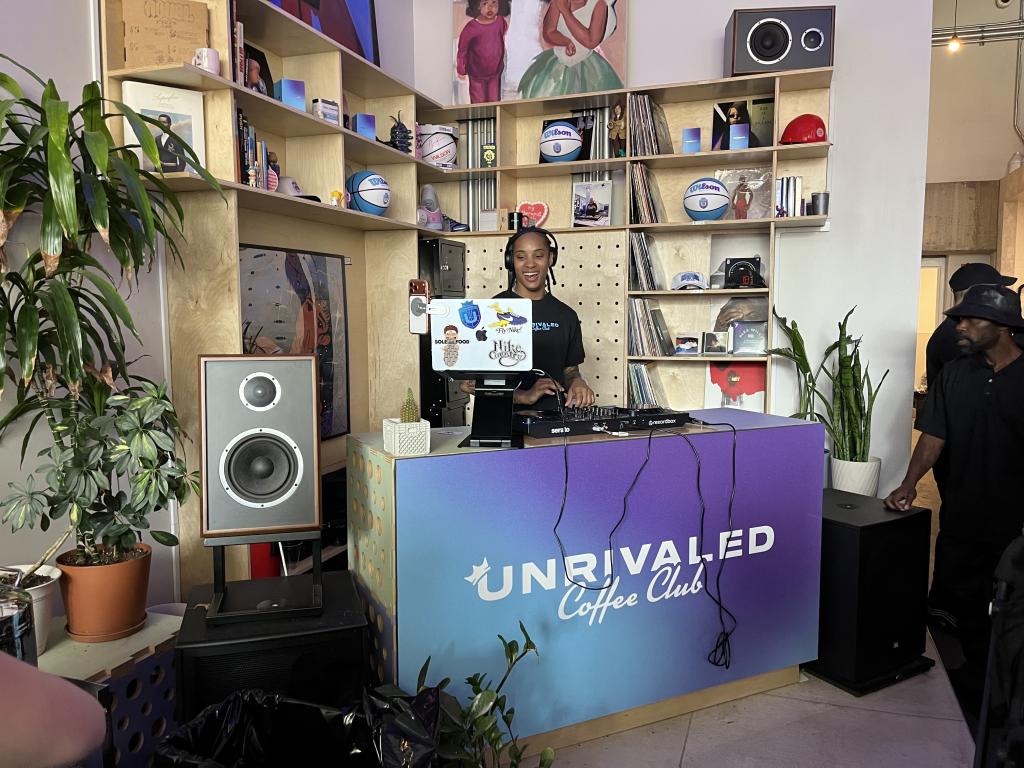A DJ in a booth branded by Unrivaled Coffee Cub