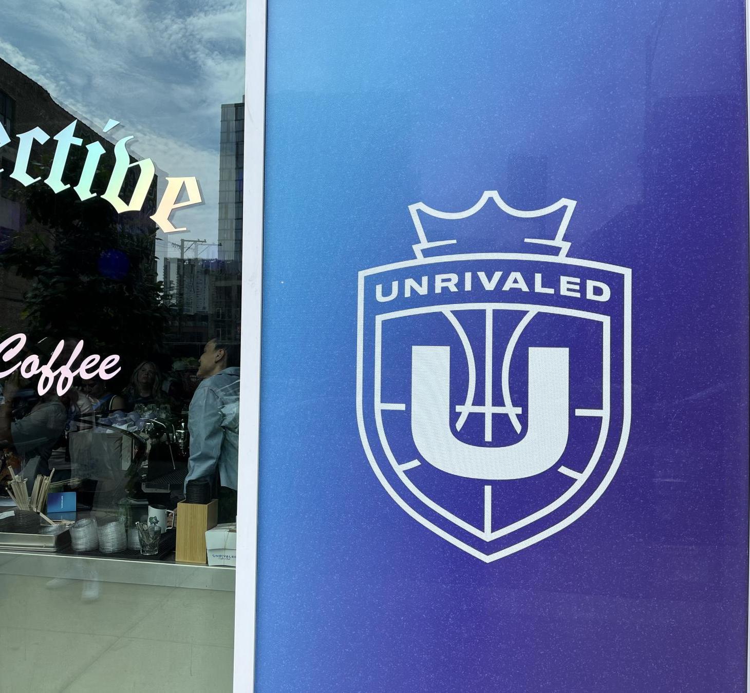 Cafe storefront window with cursive 'coffee' text and reflections of people and buildings outside; blue panel with a white crest to the right.