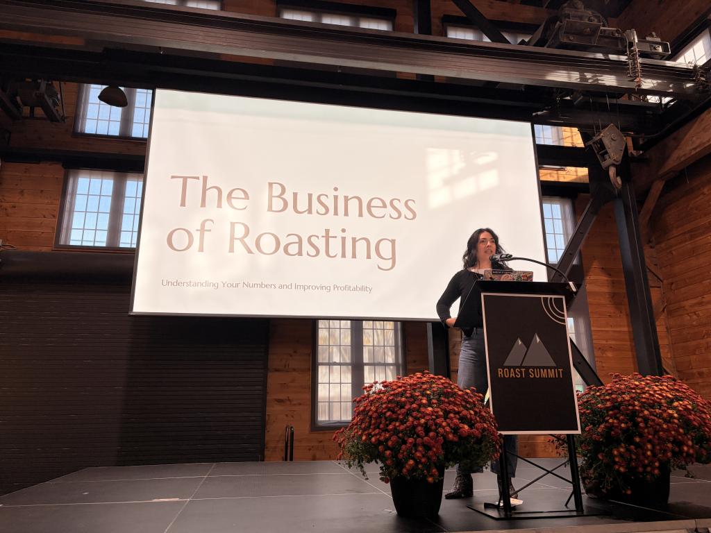 A speaker on stage in front of a screen that says 